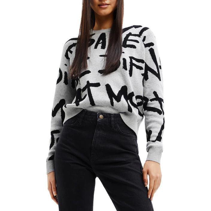 Woman wearing a GUOCALI Paris grey sweater with black graphic text, paired with black jeans